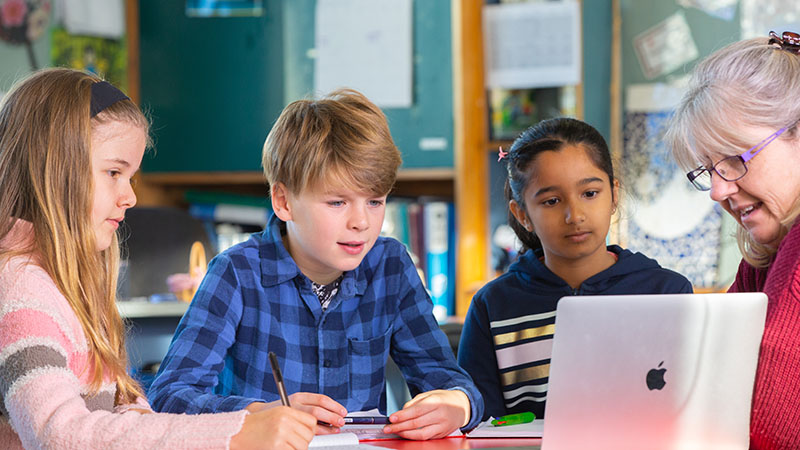 Students and their teacher looking at a laptop